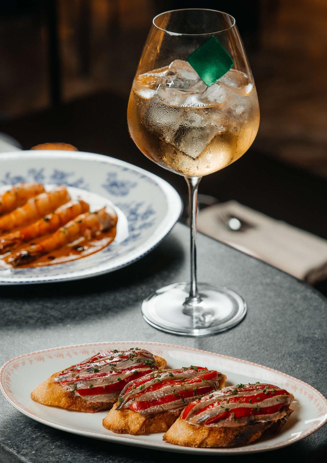 A spritz beside anchovy toasts and prawns