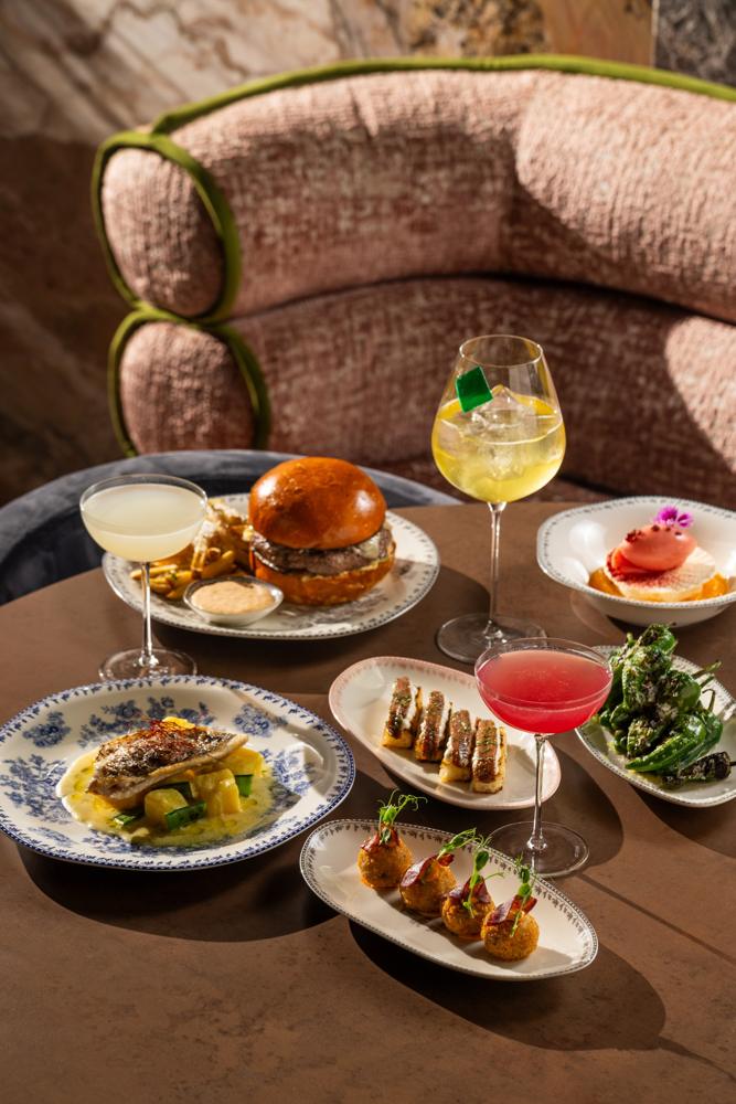 A table of dishes and cocktails in front of a velvet banquette