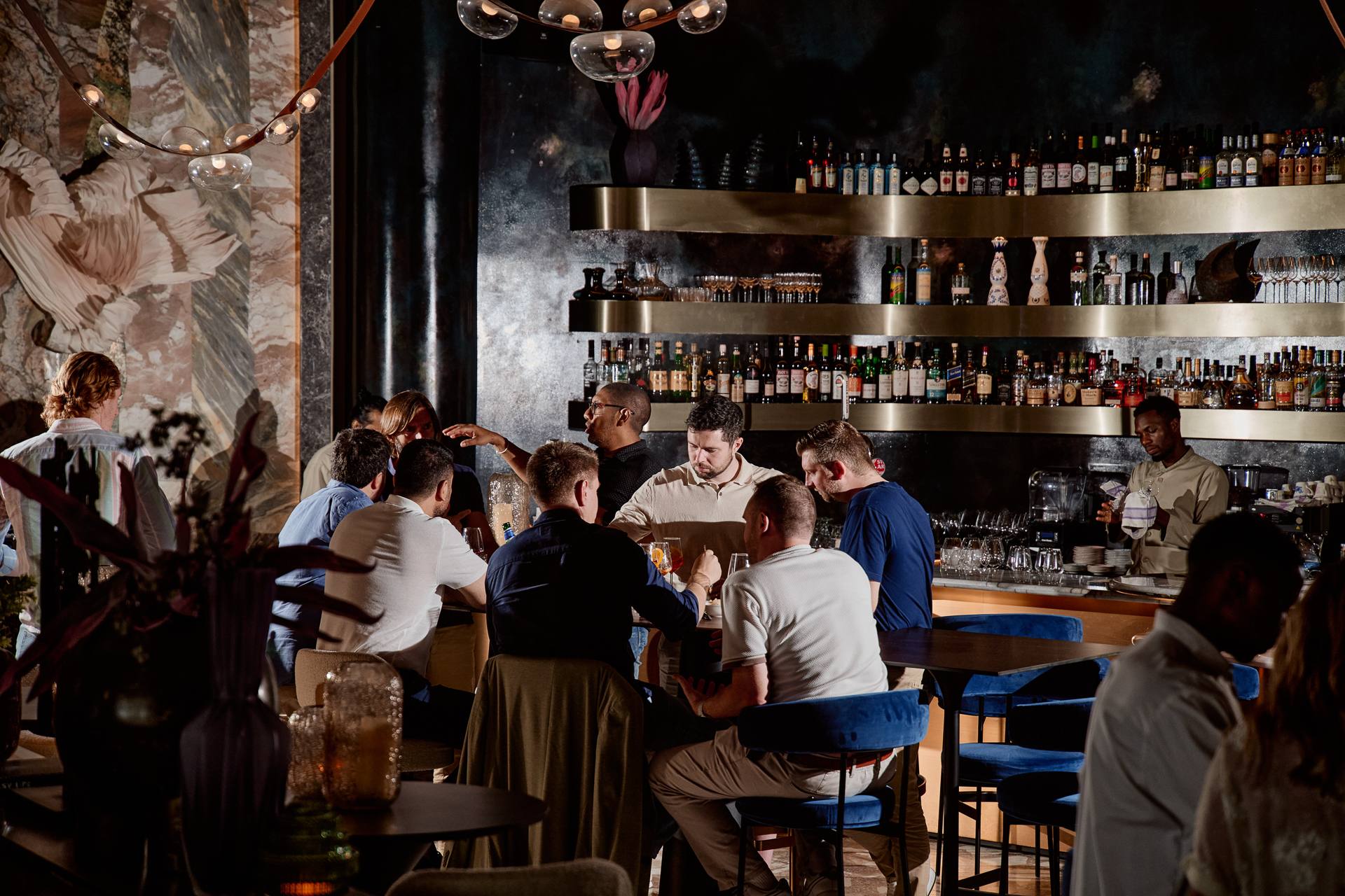 Guests at the bar at Fuoco, under the glass chandelier and brass shelves