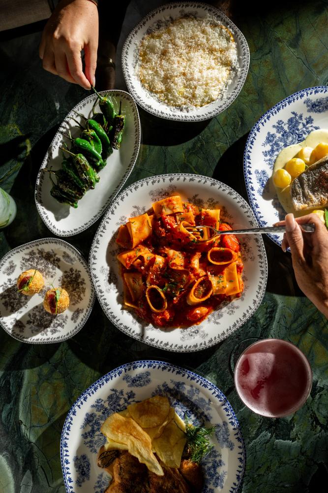 Hands reaching into shared pasta and pimientos