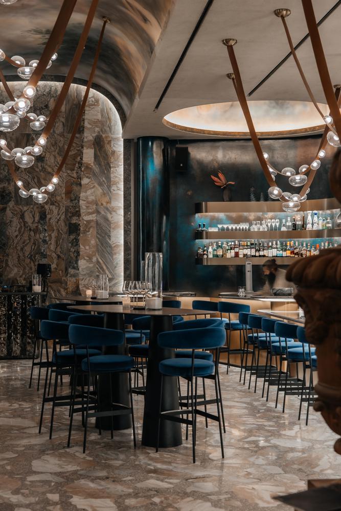 The bar at Fuoco: blue velvet stools, marble walls and glass chandeliers